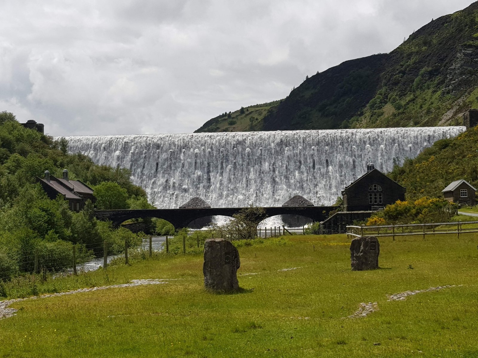 Dam wall flowing like a waterfall behind a bridge