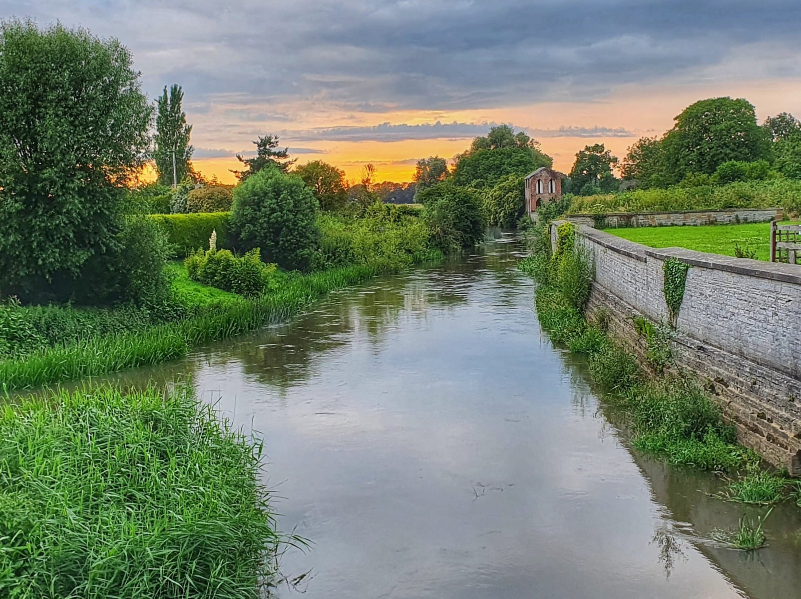 Calm river bordered by gardens at sunset